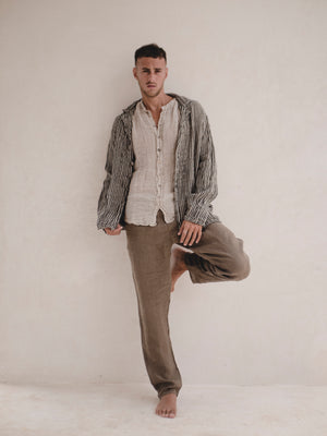 Man wearing a striped blazer over a button-up shirt with brown pants against a plain background