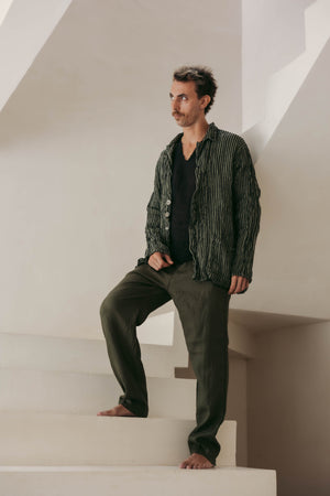 Man in a striped blazer and dark pants standing on a staircase in a minimalistic setting