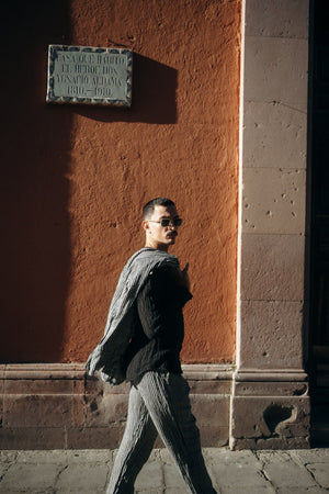 Man wearing a striped linen set walking past a textured wall with a plaque in an urban setting
