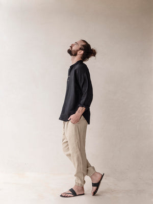 Man wearing a black shirt and beige pants against a plain background