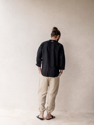 Person wearing a black linen shirt and beige pants against a plain background