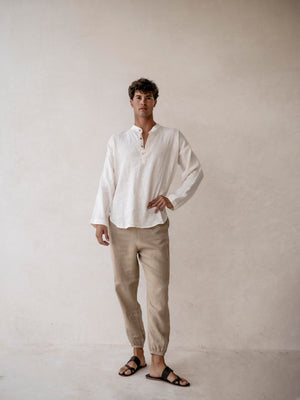 Man wearing a white shirt and beige pants against a plain background