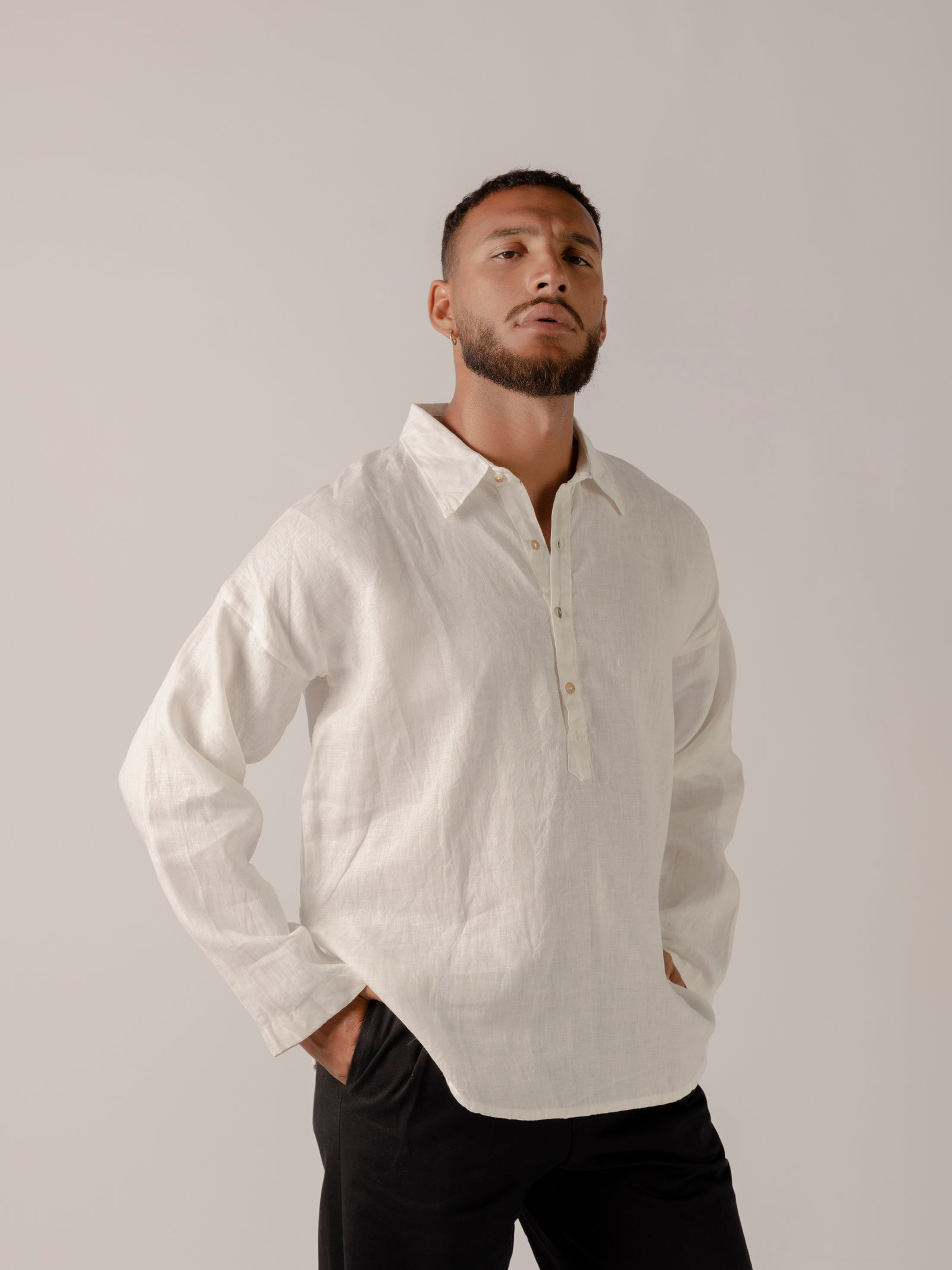 A male model wearing a white, long-sleeved, half-button placket collar shirt made of linen.