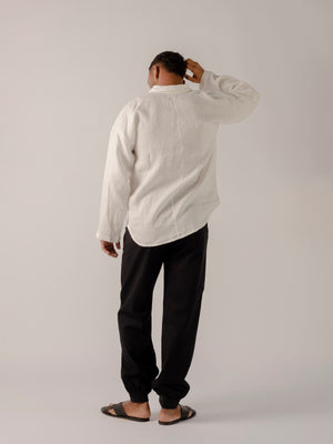 A male model wearing a white, long-sleeved, half-button placket collar shirt made of linen.