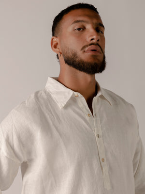 A male model wearing a white, long-sleeved, half-button placket collar shirt made of linen.