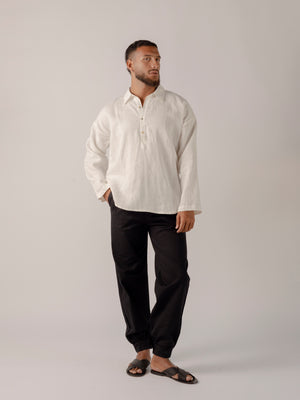 A male model wearing a white, long-sleeved, half-button placket collar shirt made of linen.