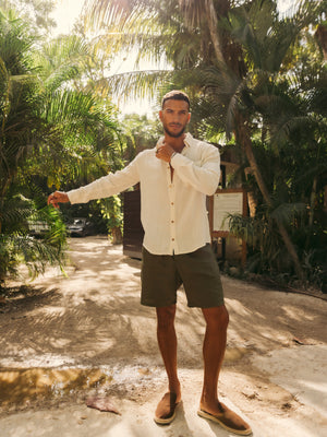 Man standing in a tropical setting with palm trees and a path.
