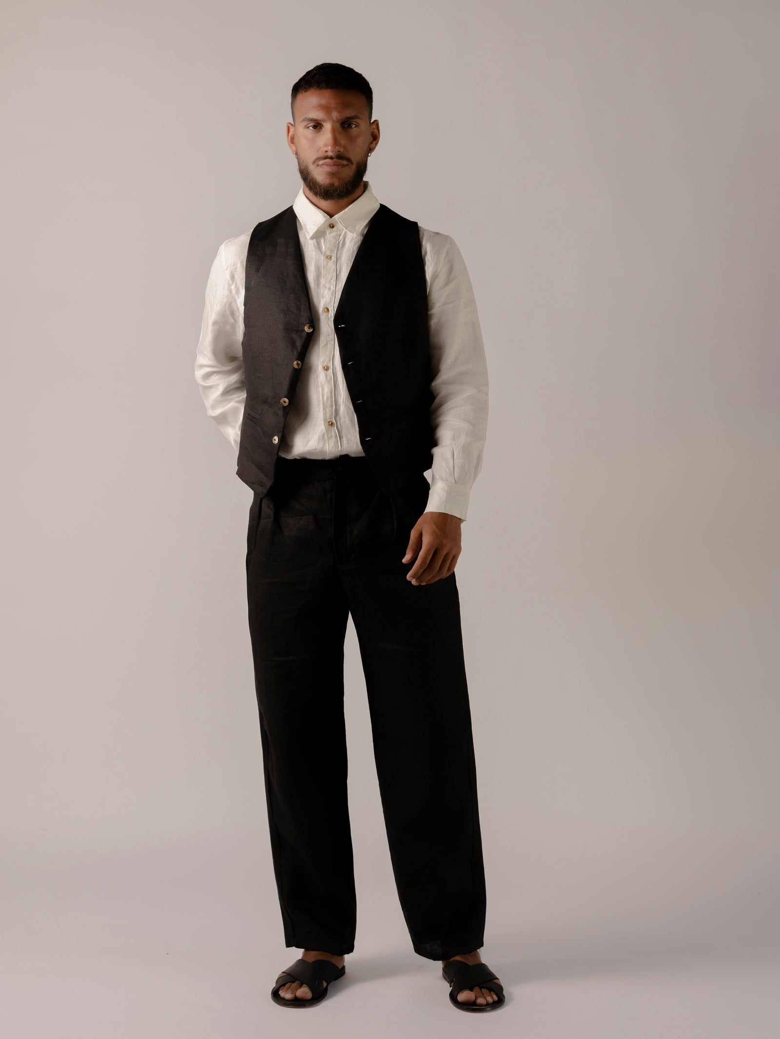 A model wearing black classic fit straight-line trousers with pockets on the sides and behind, and subtle pleat detailing from the waistband.