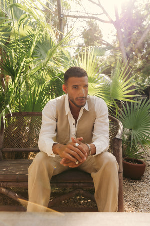 Man sitting on a bench in a garden with greenery around wearing a linen set