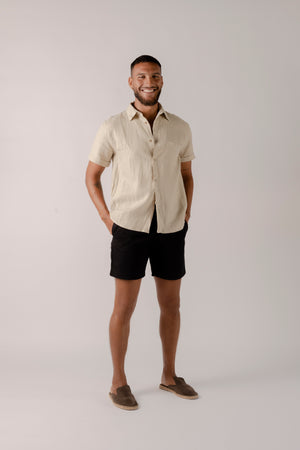 A man wearing a khaki short-sleeved button-down linen shirt with the collar buttoned up.
