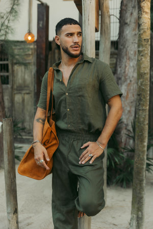 A man wearing an olive short-sleeved button-down linen shirt with the collar buttoned up.