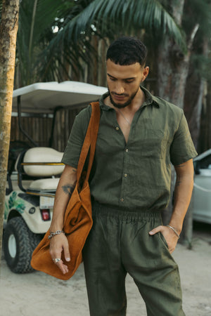 A man wearing an olive short-sleeved button-down linen shirt with the collar buttoned up.
