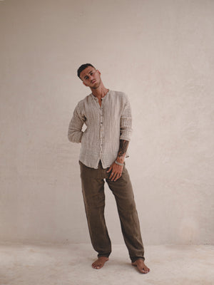 Man wearing a light-colored shirt and dark pants against a plain background