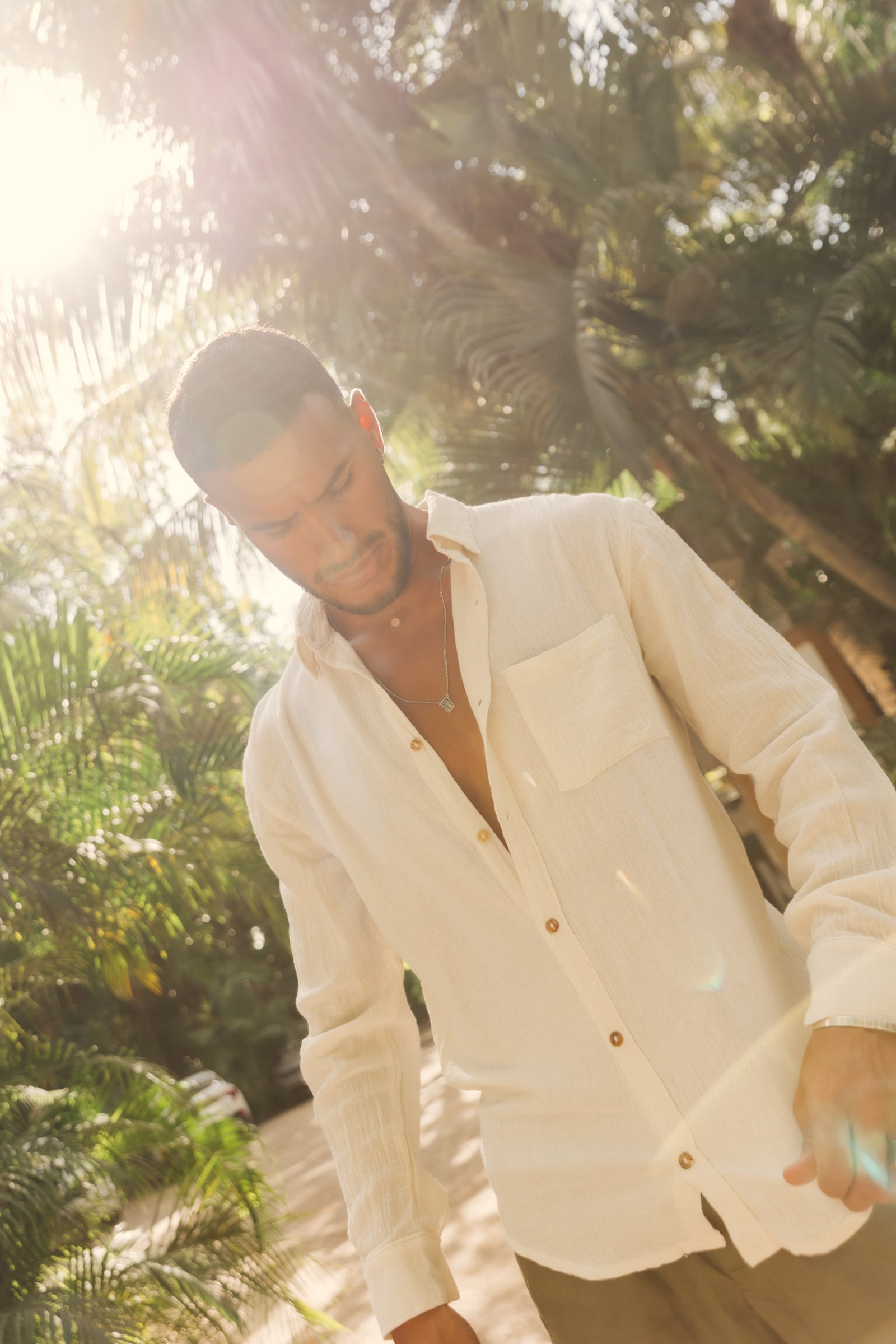 Man wearing a white shirt with gold buttons in a jungle setting
