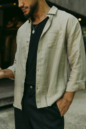 A person wearing a long sleeve khaki linen shirt with the collar buttoned up.