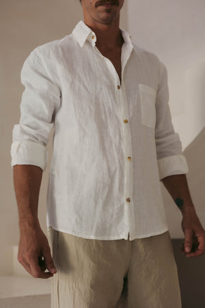 A person wearing a long sleeve white linen shirt with the collar buttoned up.