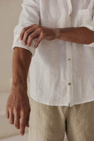 A person wearing a long sleeve white linen shirt with the collar buttoned up.