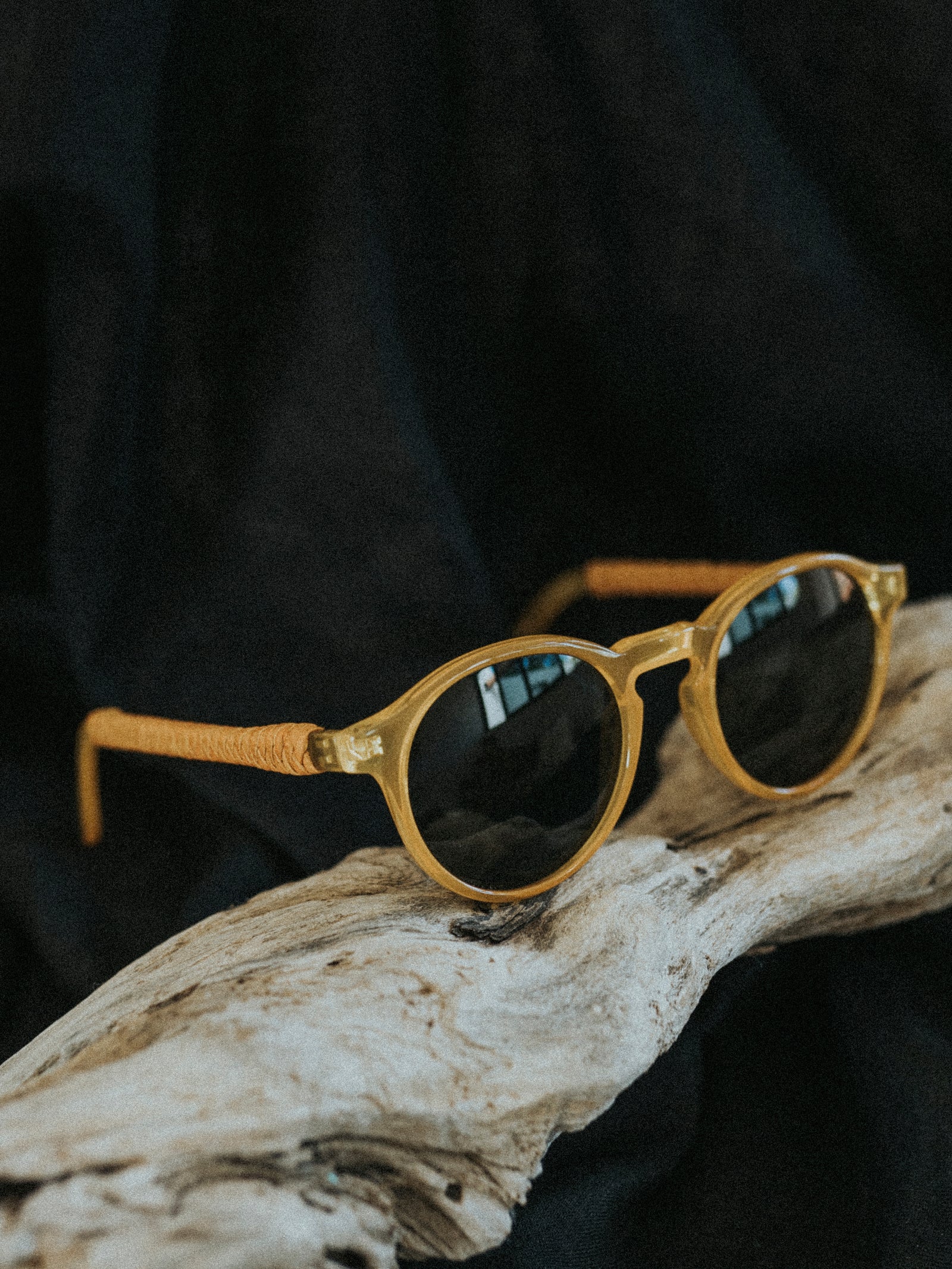 Gold-framed sunglasses with dark lenses on a wooden surface against a black background