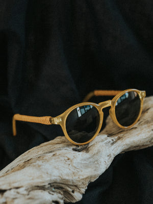 Gold-framed sunglasses with dark lenses on a wooden surface against a black background
