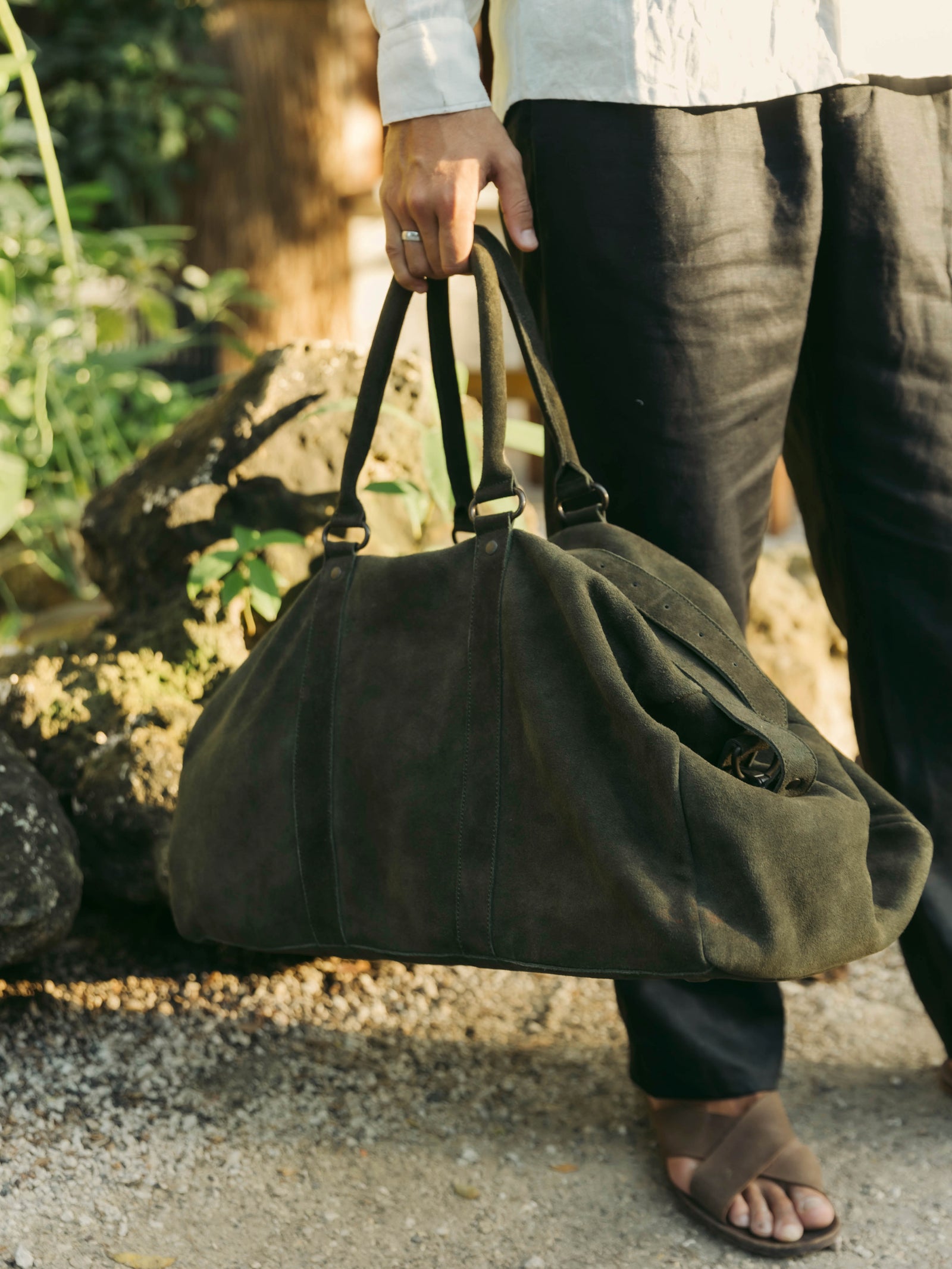 Person holding a large SUEDE LEATHER green duffle bag outdoors with blurred background