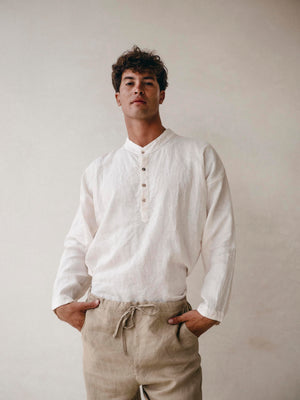 Man wearing a white linen shirt and beige pants against a plain background