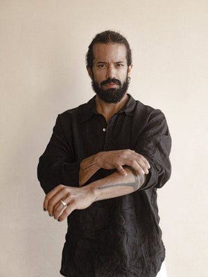 A male model wearing a black, long-sleeved, half-button placket collar shirt made of linen.
