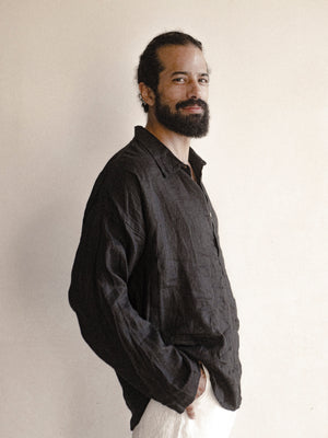 A male model wearing a black, long-sleeved, half-button placket collar shirt made of linen.