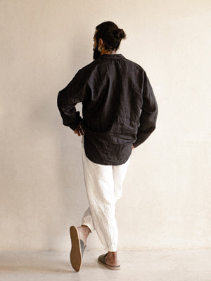 A male model wearing a black, long-sleeved, half-button placket collar shirt made of linen.