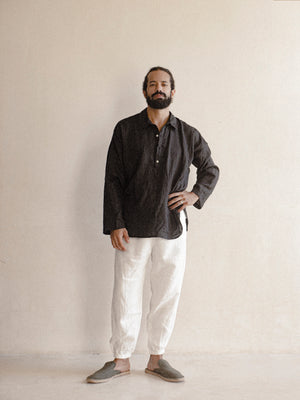 A male model wearing a black, long-sleeved, half-button placket collar shirt made of linen.
