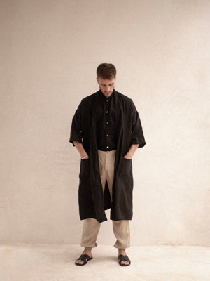 A person standing wearing a black kimono with 3/4 sleeves and pockets, paired with beige trousers.