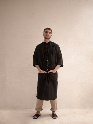 A person standing wearing a black kimono with 3/4 sleeves and pockets, paired with beige trousers.