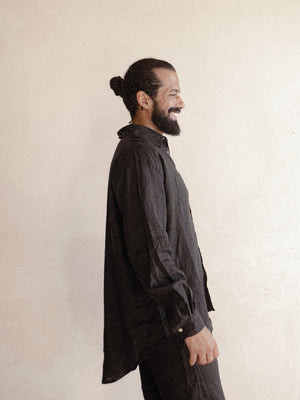 A man standing against a plain background, wearing a black oversized shirt with long sleeves.