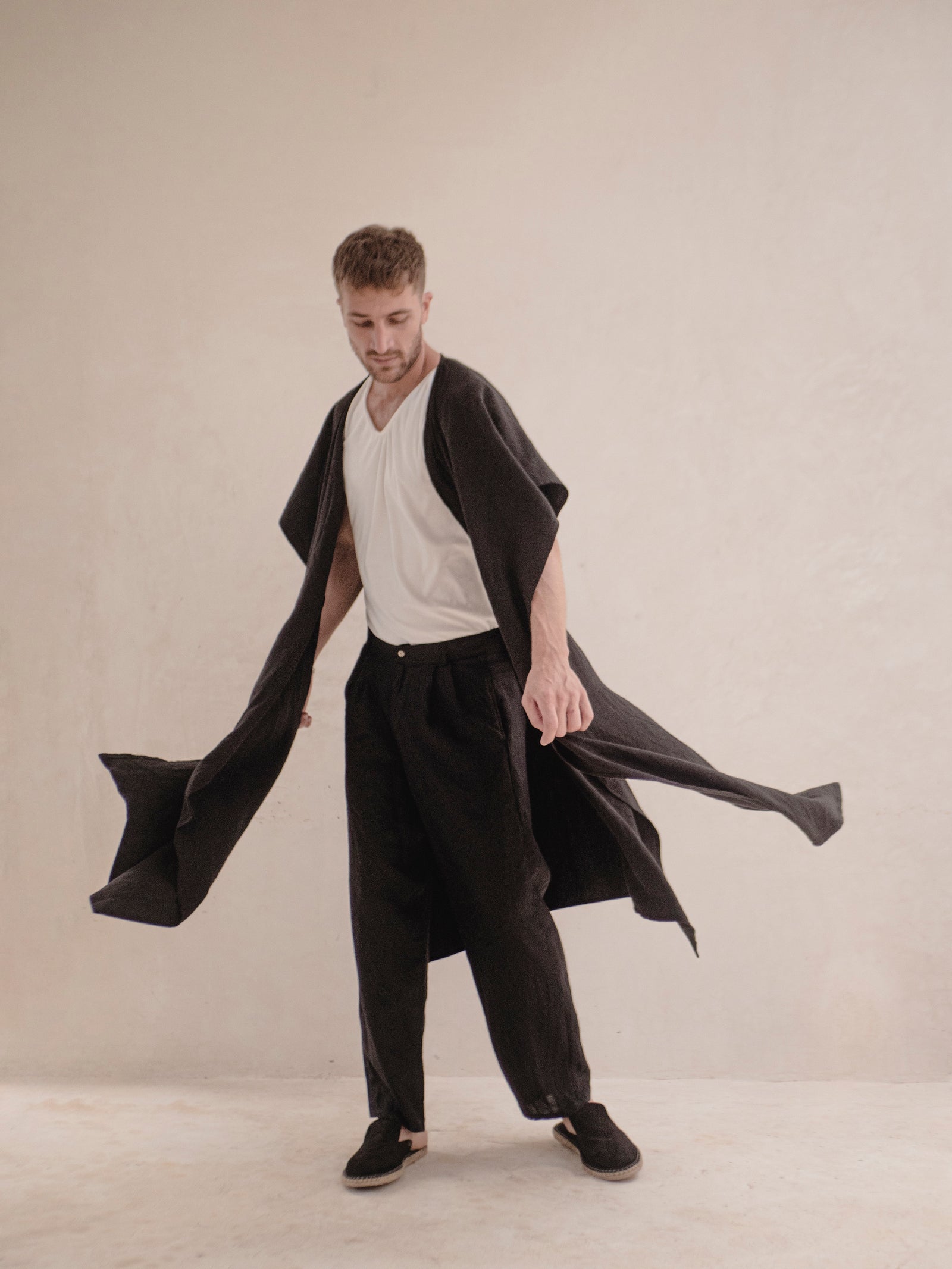 A person standing and modeling a long, black ruana with a open front, wrapped around the shoulders like a scarf.