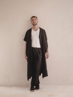 A person standing and modeling a long, black ruana with a open front, wrapped around the shoulders like a scarf.