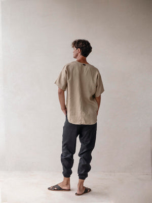 A pair of men's linen jogger pants in black, with an elasticized drawstring waist and side pockets. The pants are displayed on a model wearing sandals.