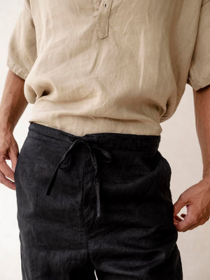 A pair of men's linen jogger pants in black, with an elasticized drawstring waist and side pockets. 