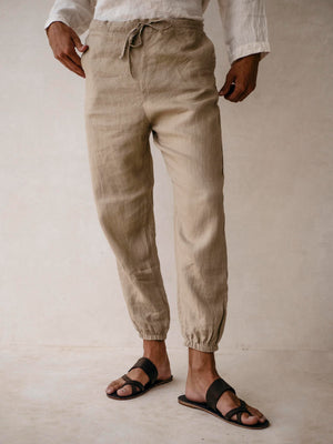 A pair of men's linen jogger pants in khaki, with an elasticized drawstring waist and side pockets. 