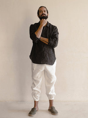 A pair of men's linen jogger pants in white, with an elasticized drawstring waist and side pockets. 