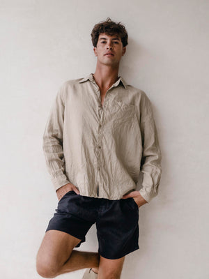 A man wearing black linen bermuda shorts with elasticized waist and side pockets. He is also wearing a light-colored shirt.