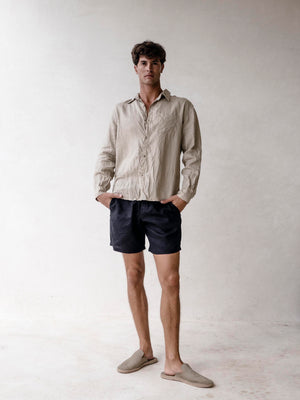A man wearing black linen bermuda shorts with elasticized waist and side pockets. He is also wearing a light-colored shirt.