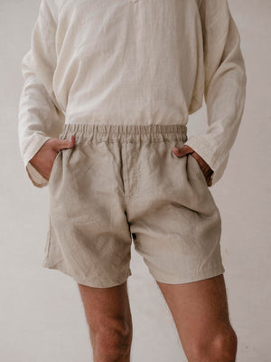 A man wearing khaki linen bermuda shorts with elasticized waist and side pockets. 
