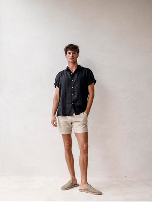 A man wearing a black short-sleeved button-down linen shirt with the collar buttoned up.