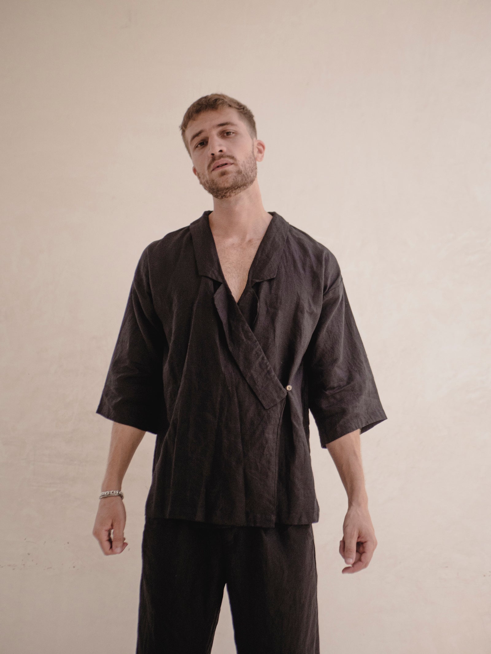 A person wearing a black kimono with 3/4 sleeves and a collar lapel, standing against a neutral background.