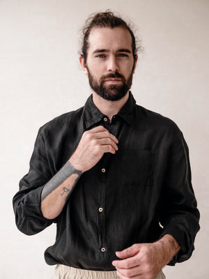 A man wearing a long sleeve black linen shirt with the collar buttoned up.